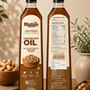 Two bottles of Meadow's Wood-Pressed Groundnut Oil are shown side by side on a wooden surface, displaying the front and back labels. The bottles are filled with golden-brown oil and are surrounded by peanuts in bowls, with a soft-focus background of green leaves and a beige vase.